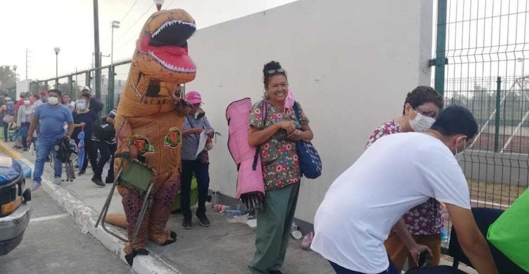 Hombre vestido de dinosaurio acompaña a su madre a vacunarse contra el Covid-19